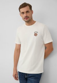 Weißes T-Shirt mit kurzen Ärmeln und rundem Halsausschnitt, mit einem gestickten Brezel-Graphic und dem Text "BISS MICH!" auf der linken Brust.
