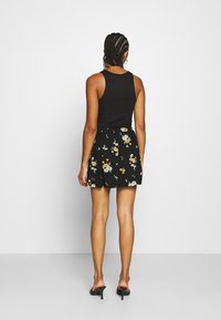 Zwarte tanktop gecombineerd met een zwarte bloemenrok met gele en grijze patronen. De rok heeft een elastische tailleband en een uitlopende vorm.