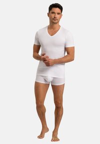 Bílá košile s výstřihem do V a krátkým rukávem, kombinovaná s bílými přiléhavými boxerkami, obojí vyrobené z měkké, elastické tkaniny, která vykazuje hladkou strukturu.