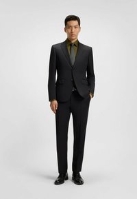 Zwarte pak met een getailleerd ontwerp, gecombineerd met een donkergroen overhemd en een zwart met stippen stropdas. Slim-fit broek en gepolijste zwarte schoenen maken de look compleet.