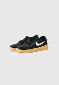 Sapatos desportivos pretos com materiais em malha e camurça, apresentando um logótipo Nike branco, sola de borracha em tom de caramelo e um design de atacadores texturizados.