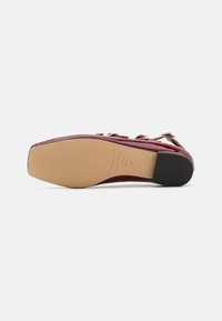 Roter Lacklederschuh mit spitzer Zehe, mittelhohem Absatz und goldenen Hardware-Akzenten. Die Sohle ist strukturiert mit einer glatten Oberfläche.