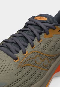 Κοντινό πλάνο γκρι και πορτοκαλιού παπουτσιού τρεξίματος Saucony που δείχνει τα κορδόνια, το αναπνεύσιμο πάνω μέρος από δίχτυ και το λογότυπο στο πλάι.