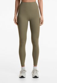 Leggings ribbed de culoare verde măsliniu, cu talie înaltă, având o textură netedă. Aferente cu adidași de culoare gri deschis și șosete albe.