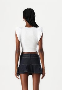 Top corto blanco acanalado con mangas rizadas combinado con una falda mini de mezclilla oscura acampanada que presenta un diseño en capas y detalles de costura.