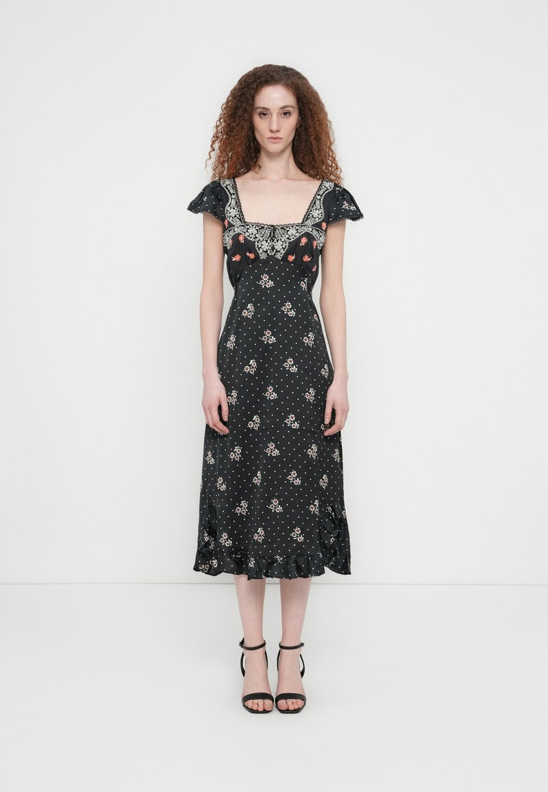 Μαύρο φόρεμα με λουλουδένιο μοτίβο, τετράγωνο ντεκολτέ, κοντά μανίκια με βολάν, μοτίβο πουά και βολάν στο τελείωμα. Συνδυασμένο με μαύρες πεδιλοφόρες γόβες με λουράκια.