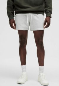Shorts en coton gris avec une taille élastique et des cordons de serrage blancs, associés à des baskets blanches et des chaussettes blanches côtelées.