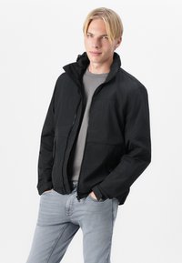 Black lightweight jacket with a high collar and zipper closure. Features two side pockets and a textured fabric for durability.