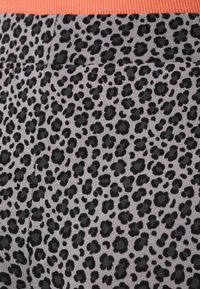 Leopard print fabric with black spots on a light gray background, featuring a ribbed coral-orange waistband. Smooth texture overall.