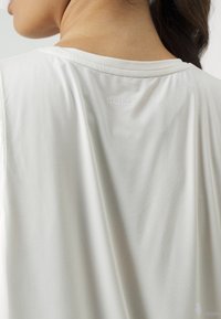 Witte sporttanktop met een gladde textuur, ronde halslijn en het woord "STRONGER" in lichtgrijs op de bovenrug gedrukt.