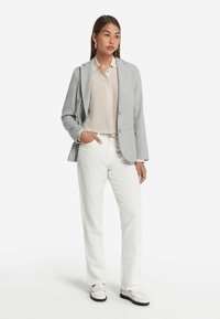 Grå texturerad kavaj över en beige blus, tillsammans med vita raka byxor och vita loafers. Har en avslappnad passform och enkel design.