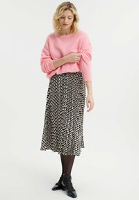 Jasnoróżowy sweter dzianinowy z długimi rękawami, zestawiony z czarną i kremową plisowaną spódnicą midi w deseń. Modelka ma na sobie czarne buty Mary Jane.