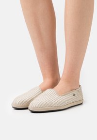 Beige vävda slip-on skor med en texturerad ovandel, rund tå och kontrasterande kant. Har en liten logotypdetalj på sidan.