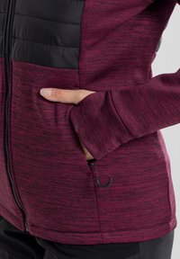 Fleece jacket in burgundy with a textured finish, featuring a black padded upper section, zip pockets, and thumbhole cuffs.