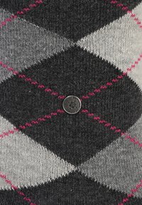 Maglione lavorato a maglia con motivo argyle in nero, grigio e bianco, con dettagli in rosa e un bottone metallico con marchio. Morbido al tatto.