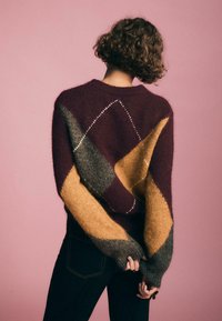 Maglione lavorato a maglia con motivi geometrici in blocchi di colore bordeaux, senape e grigio. Tessuto morbido con scollatura a coste e maniche lunghe.