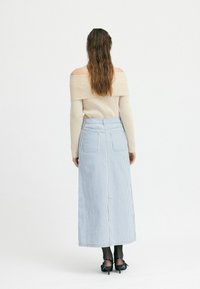 Beiger, schulterfreier, gerippter Pullover und blauer, gestreifter Maxirock mit Taschen, von hinten gezeigt. Schwarze, hohe Schuhe sind sichtbar.