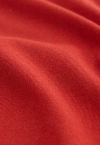 Bomullstyg i en livlig röd färg, med en slät textur som har fin ribbing och en subtil glans. Inga synliga mönster eller accenter.