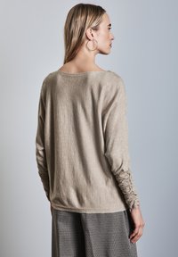 Maglione beige a maniche lunghe con una vestibilità comoda e dettagli arricciati sulle maniche, abbinato a pantaloni a vita alta con fantasie.