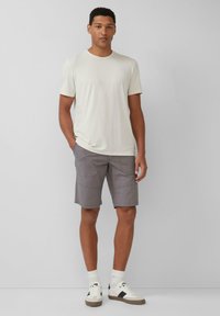 T-shirt crème à manches courtes associé à un short cargo gris. Le short présente des poches latérales ; les chaussures sont blanches avec des accents gris et des chaussettes rayées.