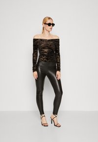 Top nero off-the-shoulder tempestato di paillettes con maniche lunghe, abbinato a leggings neri lucidi e tacchi neri con cinturino. Occhiali da sole indossati.
