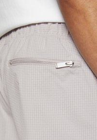 Light gray shorts with a grid pattern, elastic waistband, and a zipped back pocket featuring metallic hardware. Textured fabric.