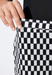 Jupe taille haute à carreaux noir et blanc avec une taille froncée, présentant un design plissé texturé et une finition en tissu lisse.