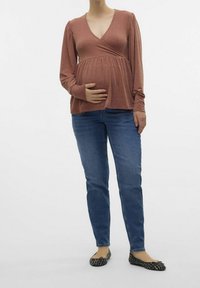 Dlouhý rukáv, hnědočervený zavinovací top s výstřihem do V a nařaseným pasem, kombinovaný s modrými džíny a černými vzorovanými balerínami.