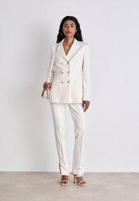 Weißes, tailliertes Blazer- und Hosen-Set. Der Blazer hat doppelte Knöpfe und große Taschen. Tragen mit Absatzsandalen und einer kleinen Tasche.