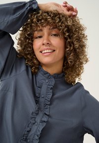 Blusa blu scuro con una parte anteriore arricciata con bottoni, maniche lunghe e scollatura elasticizzata. Texture liscia e design su misura.