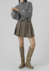 Grijze gebreide trui met hoge kraag en gestructureerde mouwen, gecombineerd met een bruine geruite geplaatste rok en kniehoge beige laarzen.