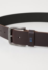 Brun læderbælte med en sølvmetal spænde, der har en læderholder med en blå og sort rektangulær detalje. Glat overflade og flad design.