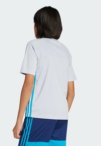 Camisa blanca de manga corta con acentos azules en los lados, con un cuello redondo y una tela suave. Combinada con pantalones cortos azules.