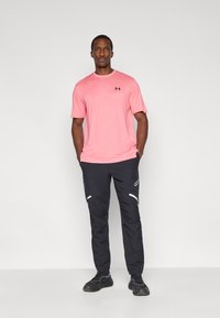 Ροζ αθλητική μπλούζα με κοντά μανίκια και λογότυπο στο στήθος, σε συνδυασμό με μαύρο παντελόνι με λευκές λεπτομέρειες και στενή γραμμή. Μαύρα αθλητικά παπούτσια.