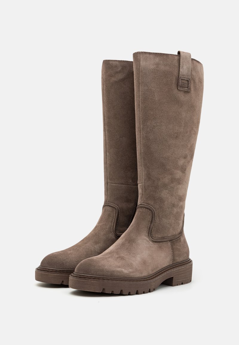 Bottes en daim marron hautes avec une texture lisse, un bout rond, et une semelle en caoutchouc robuste avec de légères rainures pour une meilleure adhérence.