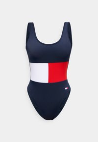 Μπλε ναυτικό ολόσωμο μαγιό με ευρεία οριζόντια λευκή και κόκκινη ρίγα στο μέσο της κοιλιάς και μικρό λογότυπο στο ισχίο.