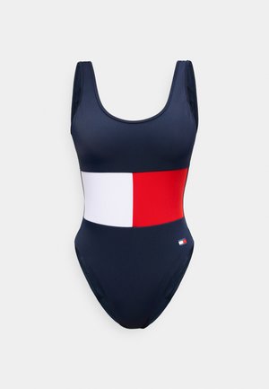 Bañador entero azul marino con una ancha franja horizontal blanca y roja en el centro y un pequeño logo en la cadera.