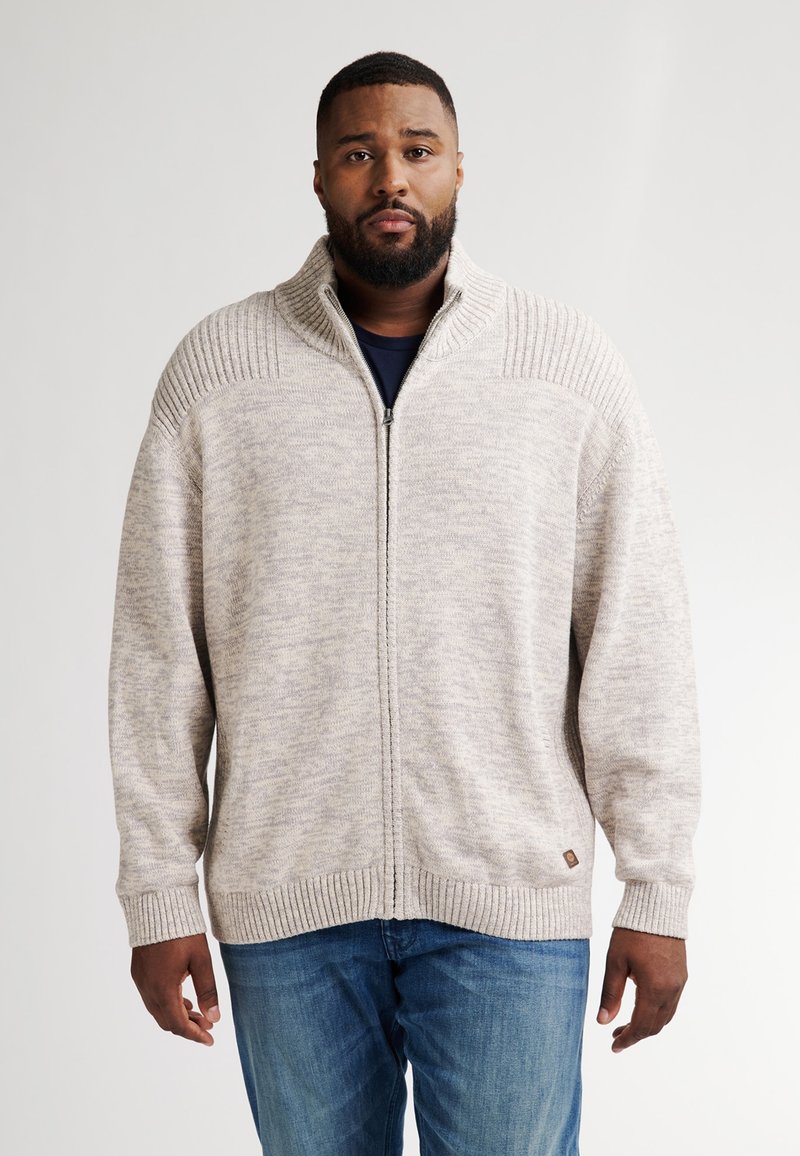 Světle béžový svetr na zip s žebrovanými detaily na ramenou a manžetách. Měkká struktura, dlouhé rukávy a uvolněný střih.