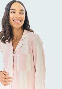 Różowo-kremowa piżama z paskami, z kołnierzykiem, długimi rękawami i kieszonką na piersi. Wykonana z miękkiego materiału, zapinana na guziki.