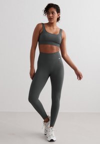 Donkergroene geribbelde sportbh en high-waisted leggings van een gladde, rekbare stof, gecombineerd met witte sportschoenen.
