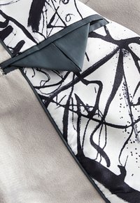 Textilmuster mit einem weichen grauen Stoff kombiniert mit einem weiß-schwarzen abstrakten Musterpaneel, akzentuiert durch dunkelblaue Kanten und Besätze.