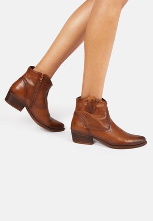 Braune Leder-Stiefeletten mit einem niedrigen Blockabsatz, seitlichem Reißverschluss, spitzer Zehenform und geprägten Details im Oberteil.