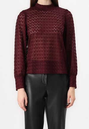 Bordeaux langærmet top med et struktureret, blonderlignende mønster og høj hals, parret med sorte læderbukser.