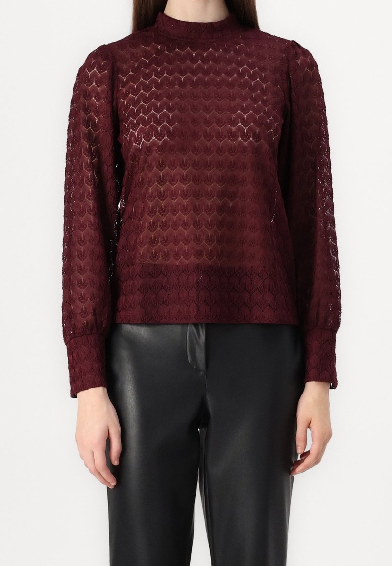 Bordeaux langærmet top med et struktureret, blonderlignende mønster og høj hals, parret med sorte læderbukser.