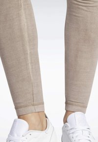 Beżowe legginsy o prążkowanej fakturze, dopasowanym kroju i kontrastowych detalach szwów, zestawione z białymi trampkami.
