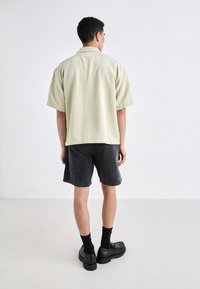 Short-sleeve, light green corduroy shirt with a relaxed fit, paired with dark gray shorts and chunky black shoes.