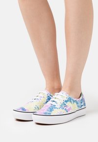 Canvas sneakers med et tie-dye mønster i pastell lilla, gul og blå. Har hvite snører og gummisåler med svart kant.