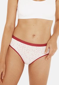 Culotte de bikini en coton blanc avec une bordure rouge, présentant un motif de petits triangles en rose, jaune et rouge. Comprend un logo sur la taille.