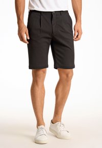 Schwarze, taillierte Shorts mit Frontfalten, aus weichem Material, mit seitlichen Taschen und umgeschlagenen Säumen, kombiniert mit weißen Sneakers.