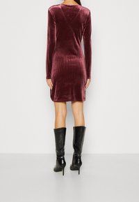 Långärmad kastanjefärgad sammetklänning med en åtsittande silhuett, med rund urringning och slät textur, kombinerad med knähöga svarta stövlar.